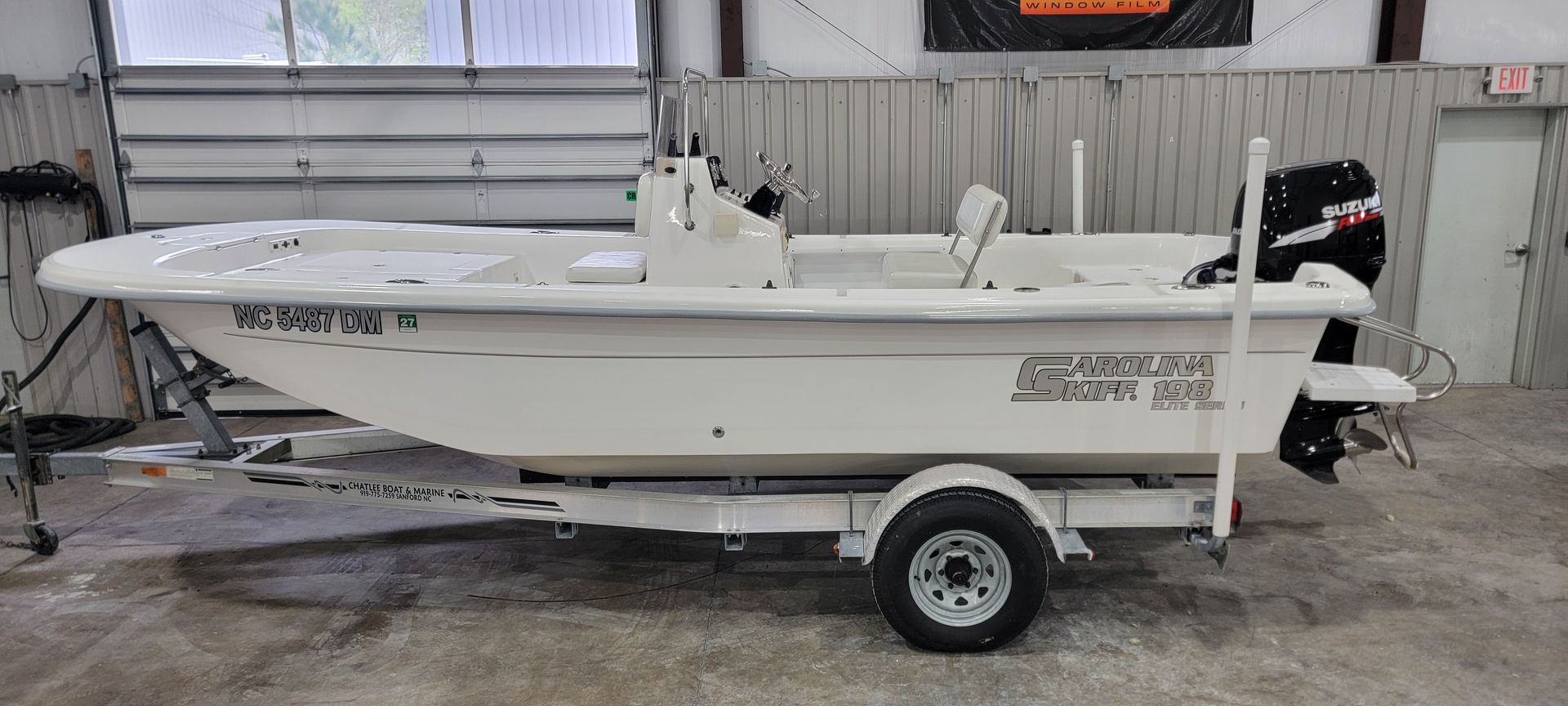 A white boat is on a trailer in a garage.