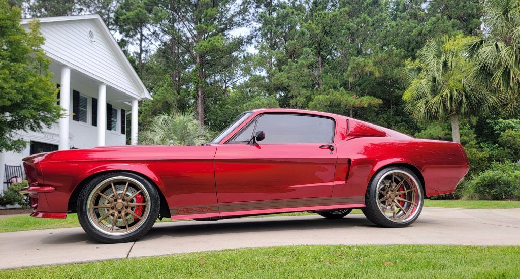A red mustang is parked in front of a white house.