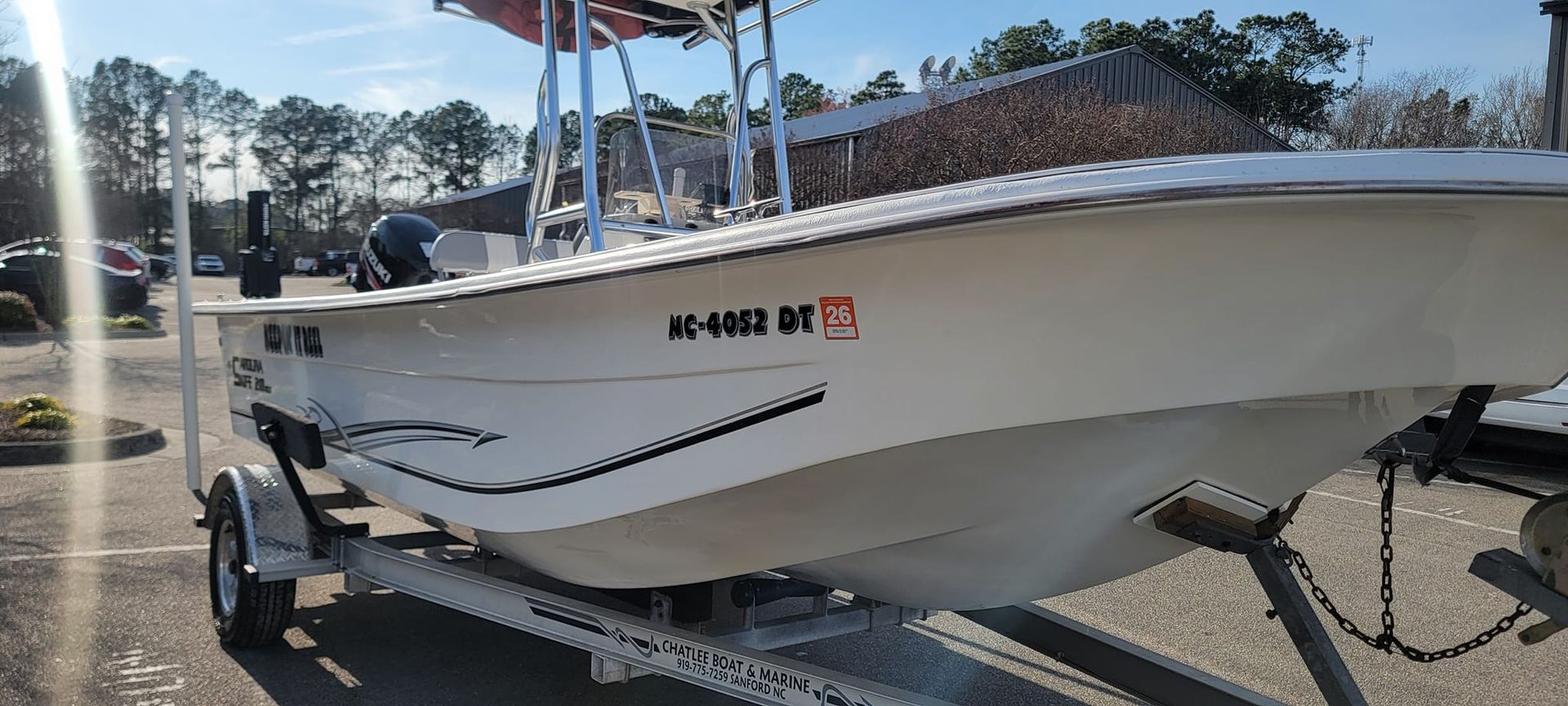 A white boat is parked on a trailer in a parking lot.
