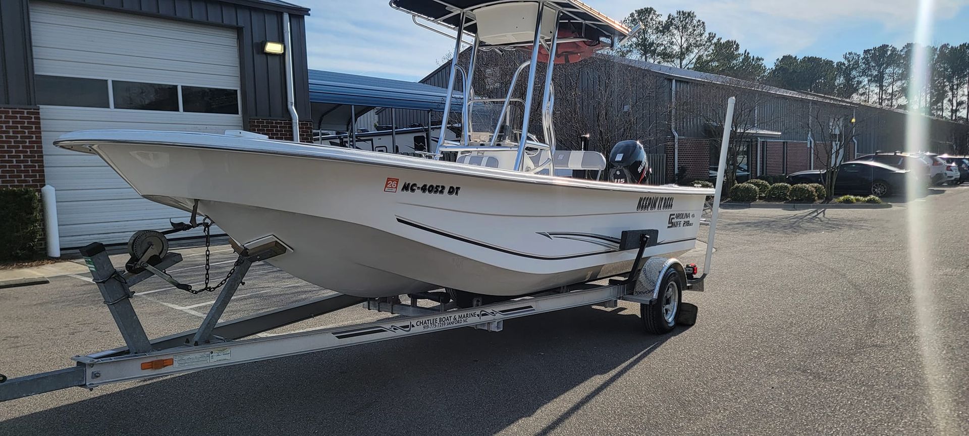A white boat is on a trailer parked in front of a garage.