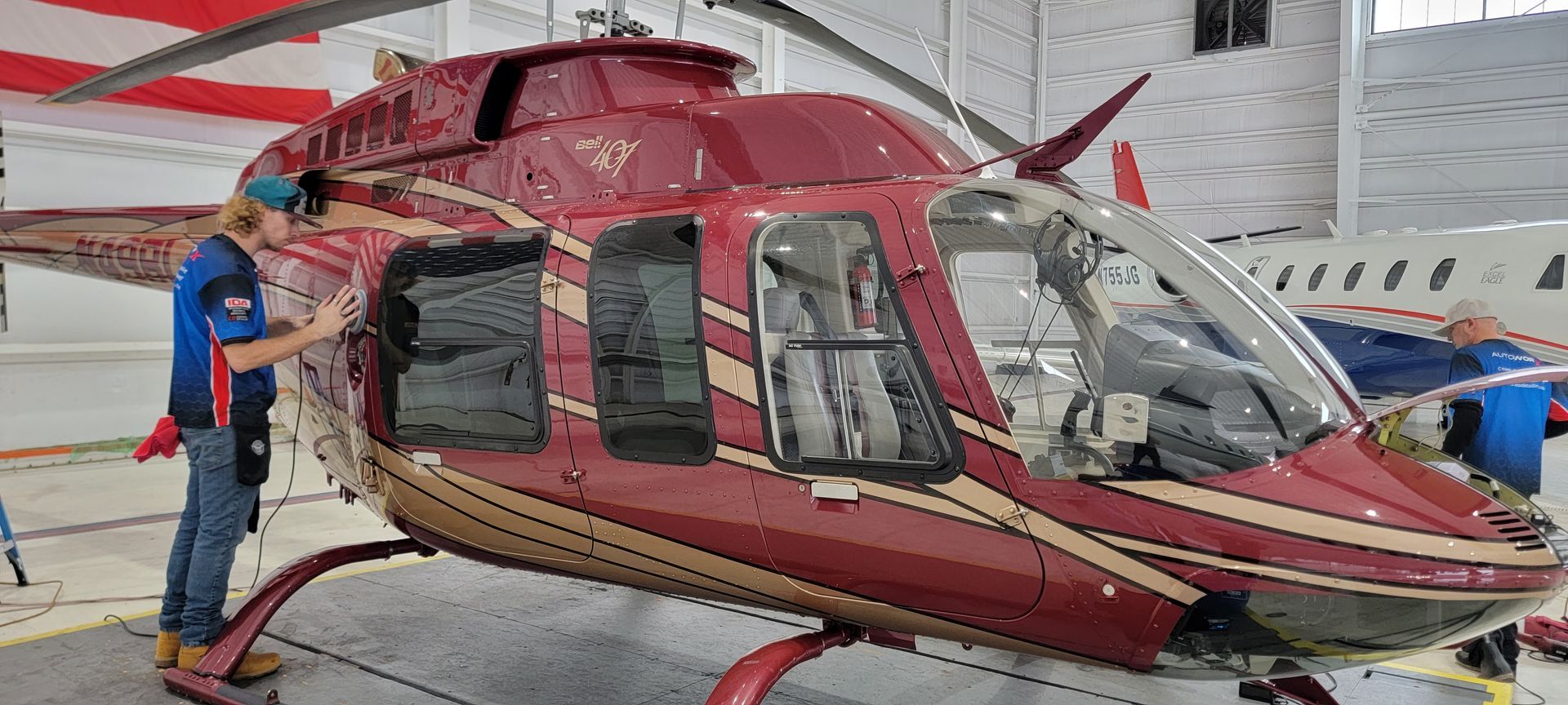 A man is working on a red helicopter in a hangar.