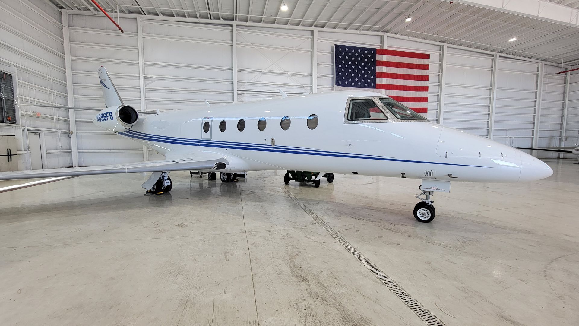 A small private jet is parked in a hangar with an american flag.