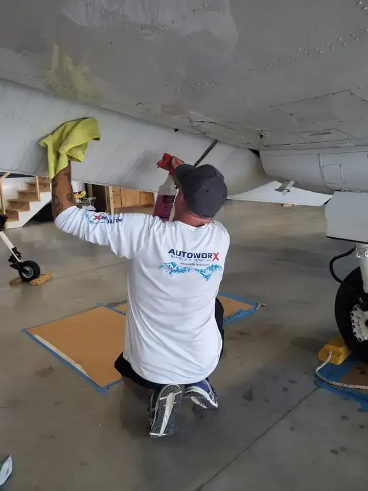 A man is kneeling down cleaning a plane in a hangar.