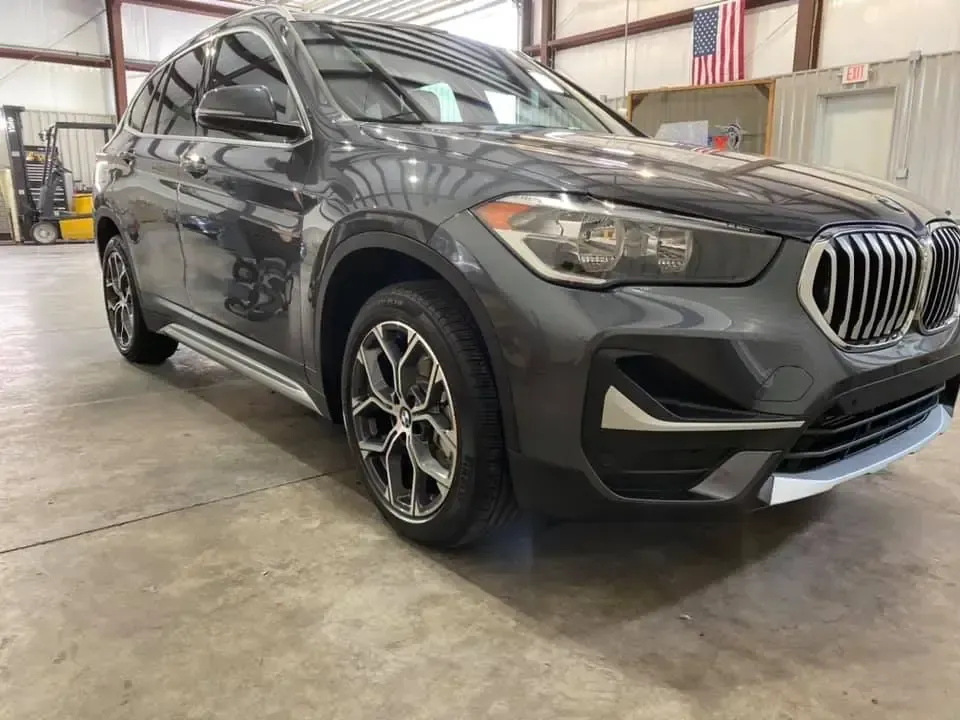 A bmw x1 is parked in a garage next to an american flag.