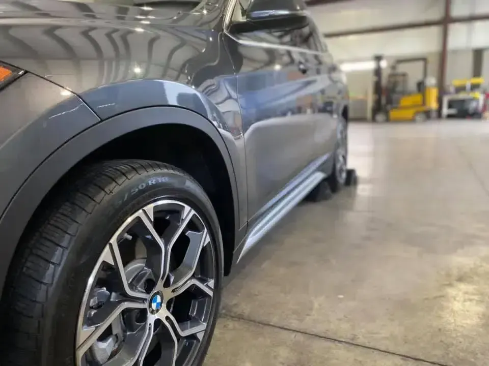 A bmw x1 is parked in a garage with a forklift in the background.