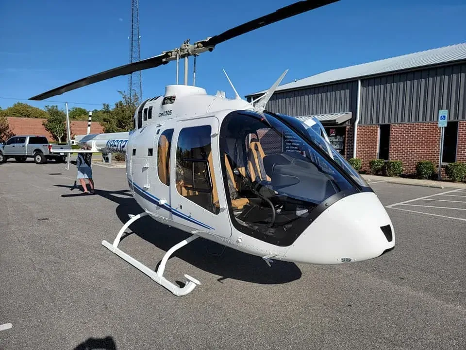 A white helicopter is parked in a parking lot in front of a building