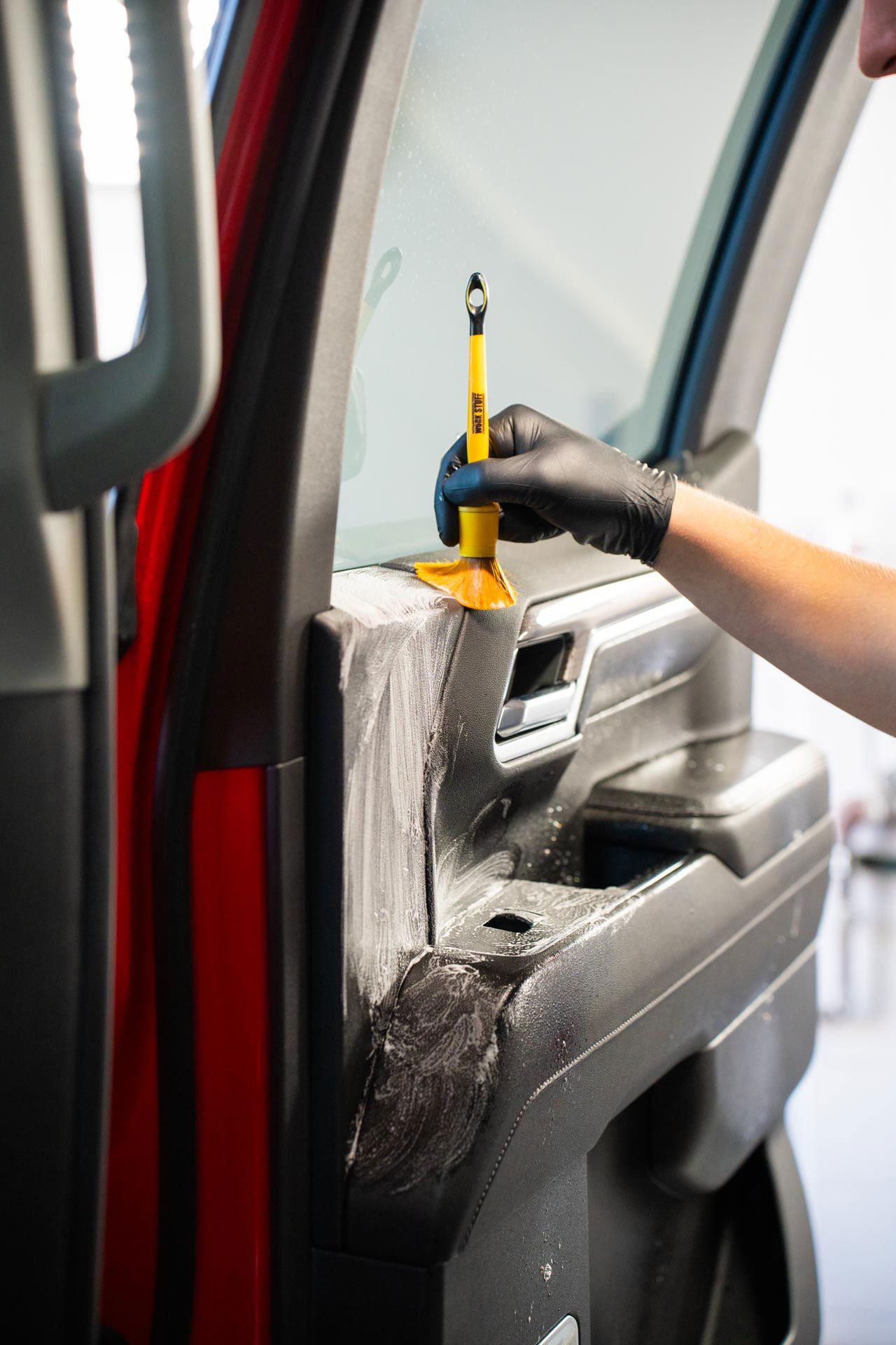 Person using a tool to apply tint to a car window, wearing a black glove. The car door is open and red.