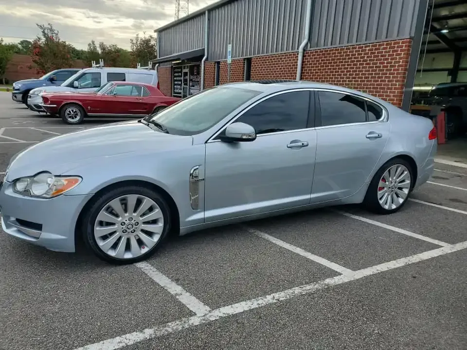 A silver jaguar f type is parked in a parking lot in front of a brick building.