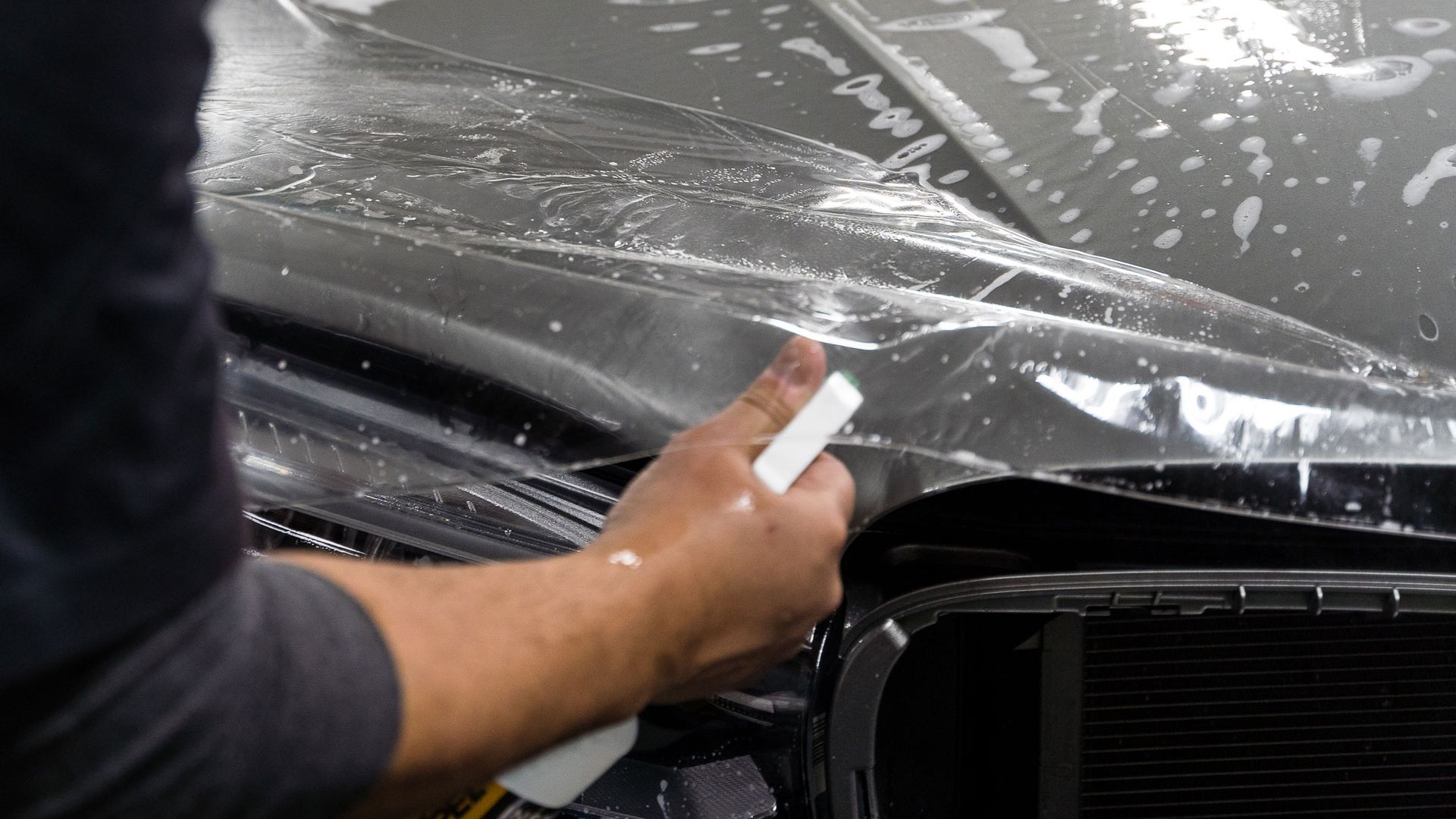 A man is applying a protective film to the hood of a car.