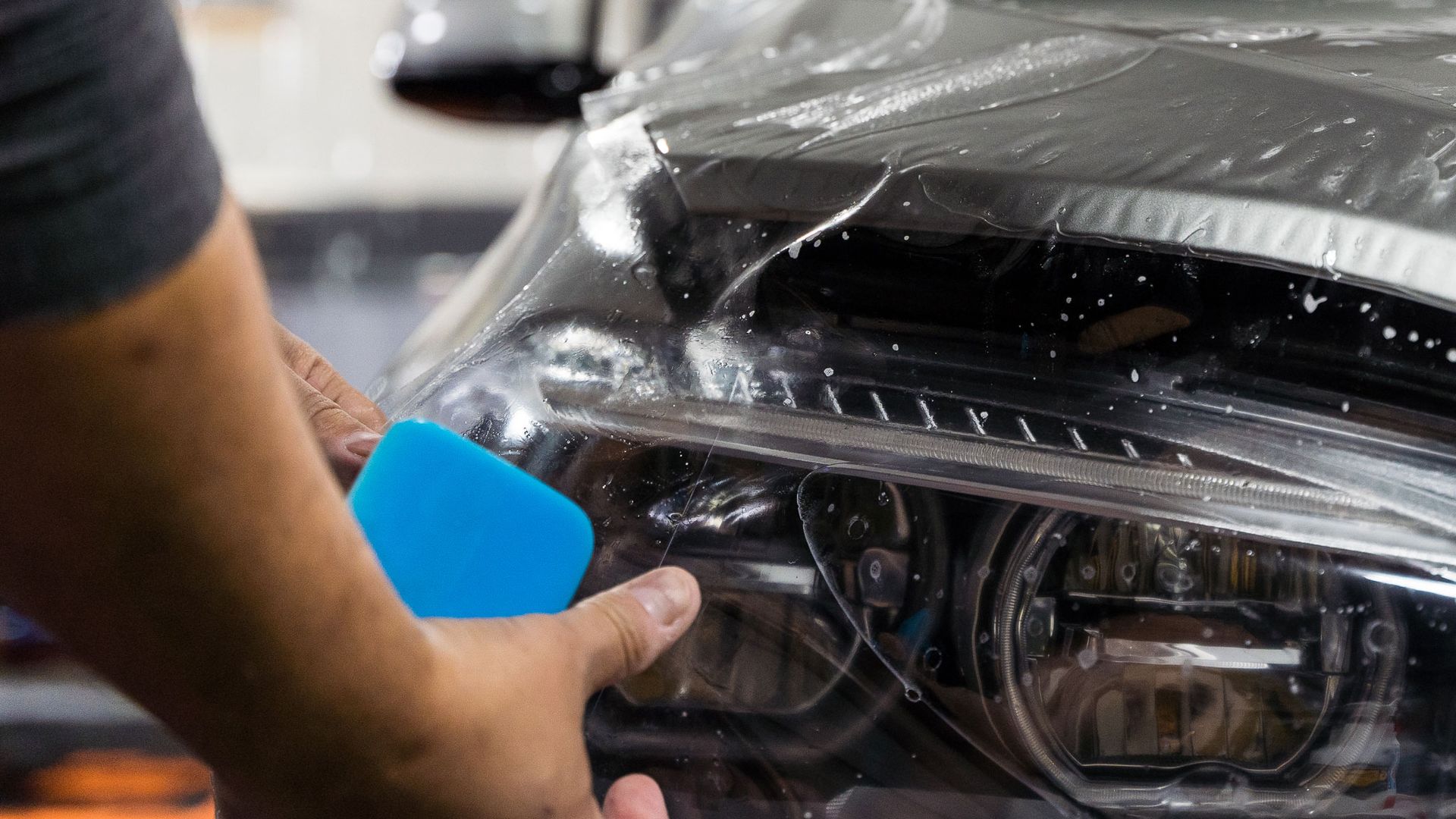 A person is applying protective film to the headlights of a car.