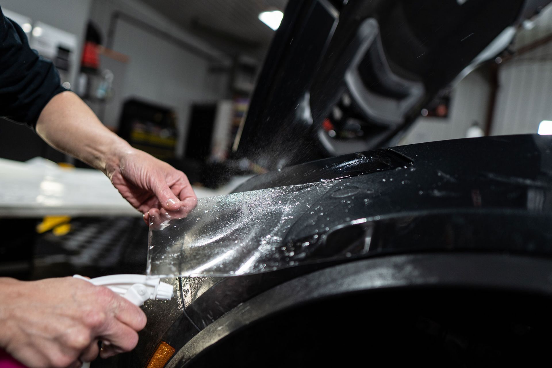 A person is applying a protective film to the fender of a car.