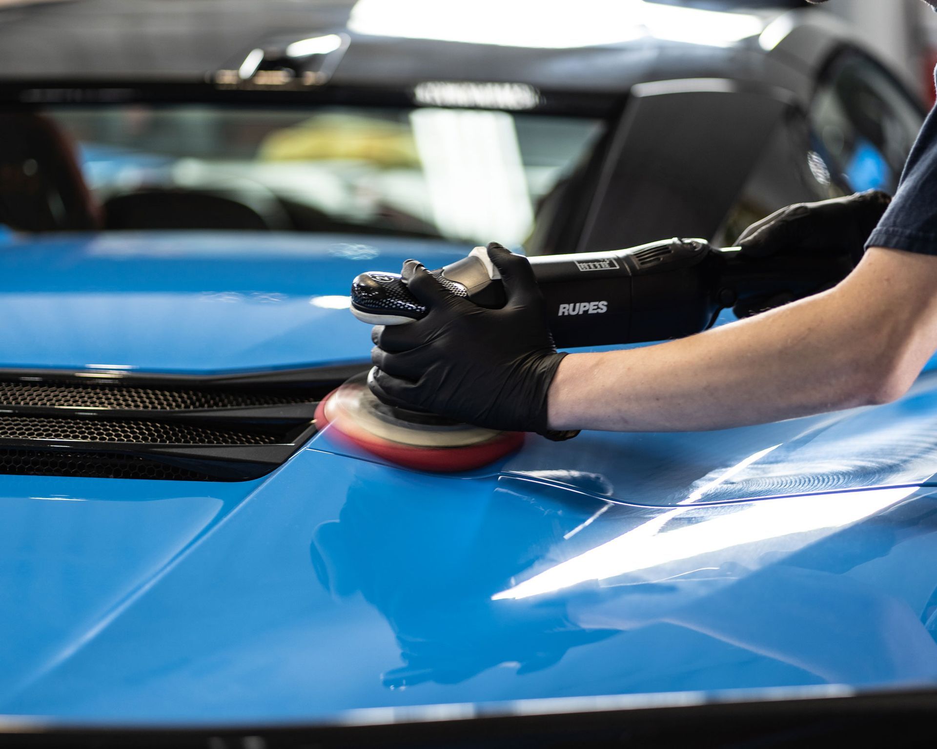 A man is polishing the hood of a blue car.