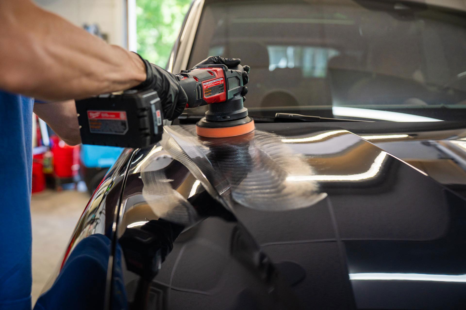 A man is polishing the hood of a black car with a machine.