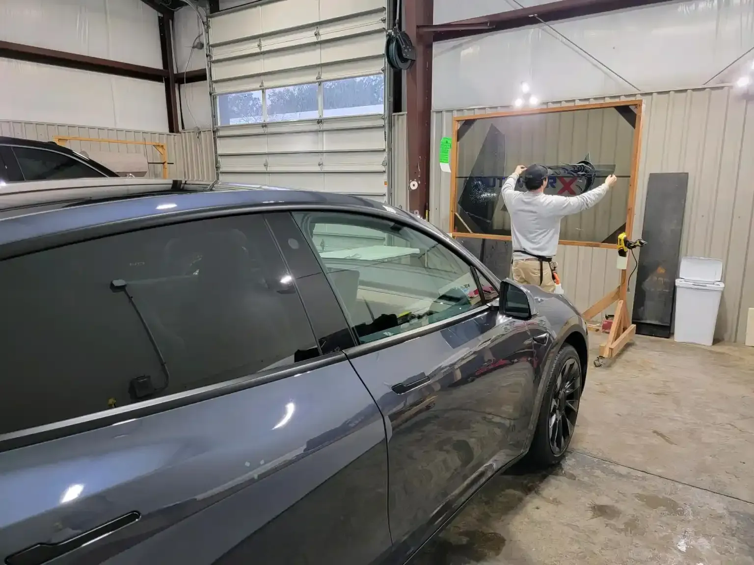 A man is installing window tinting on a tesla model s in a garage.