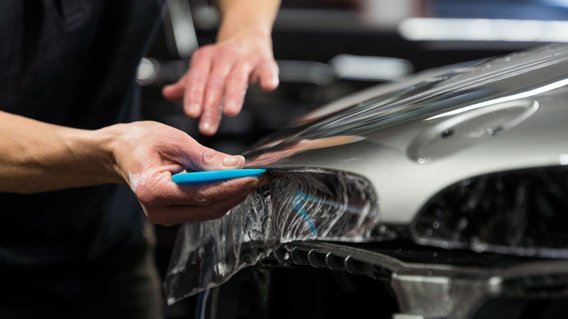 A man is applying plastic wrap to the hood of a car.
