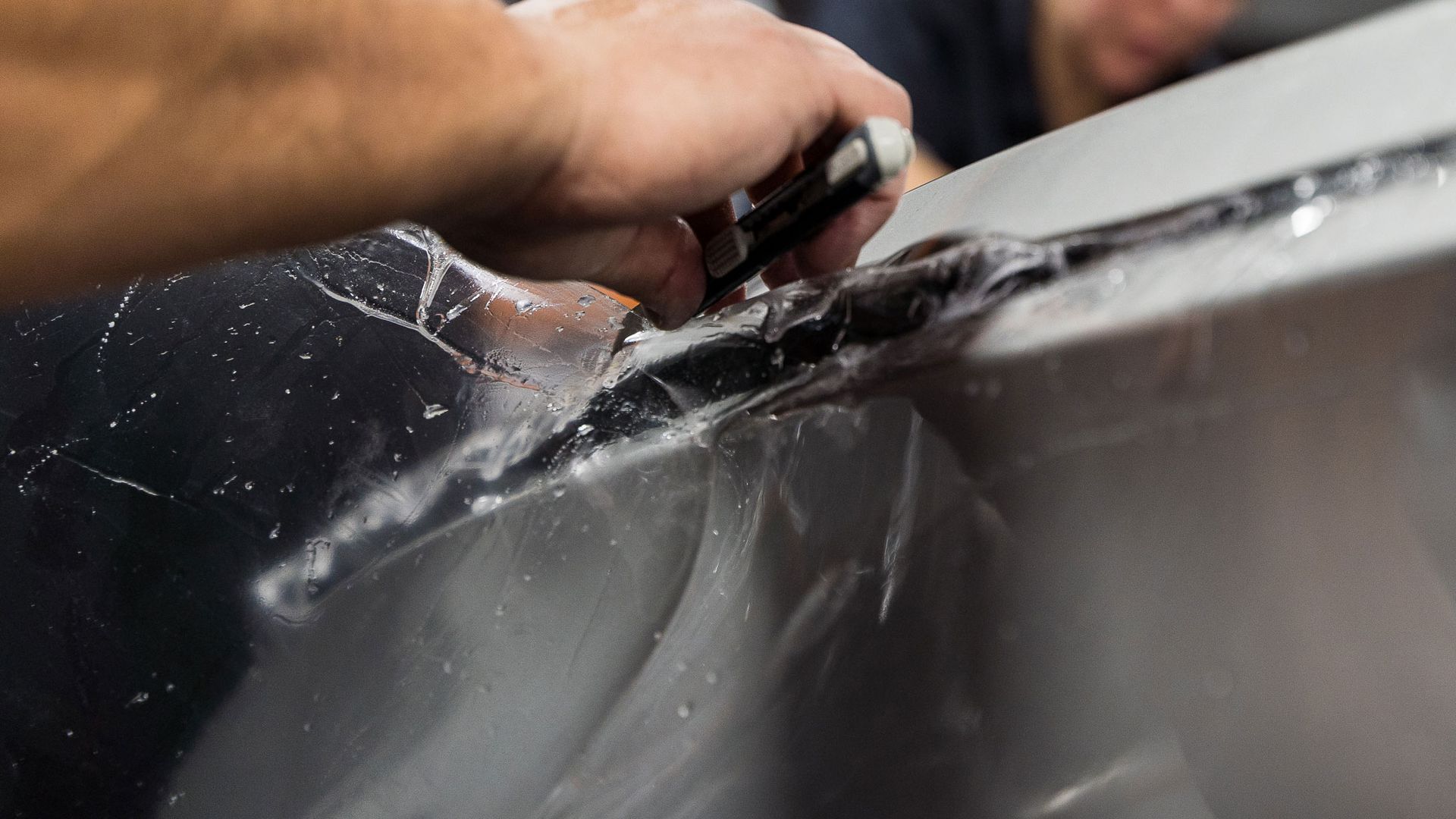 A person is cutting a piece of plastic on a car with a pair of scissors.
