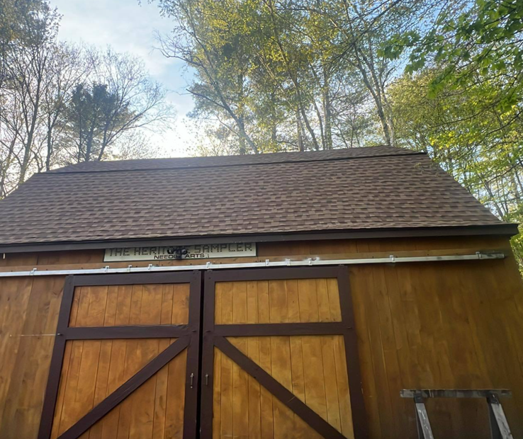 A wooden shed with a brown roof and wooden doors is surrounded by trees.
