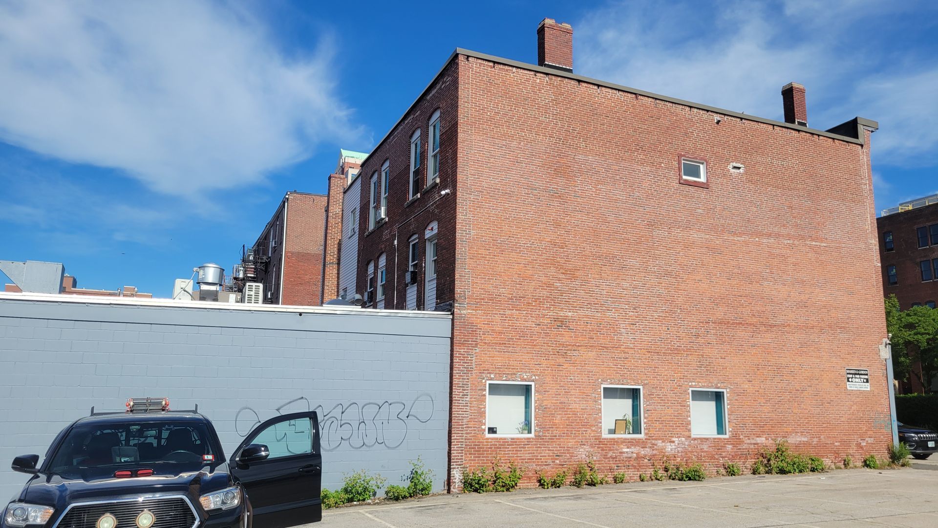 A black car is parked in front of a large brick building.