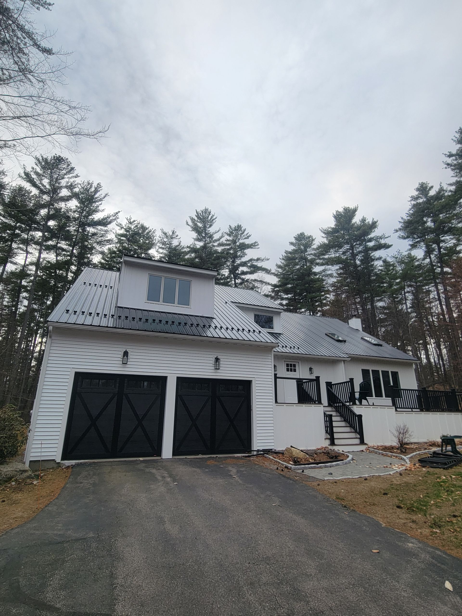 A white house with black garage doors is surrounded by trees.