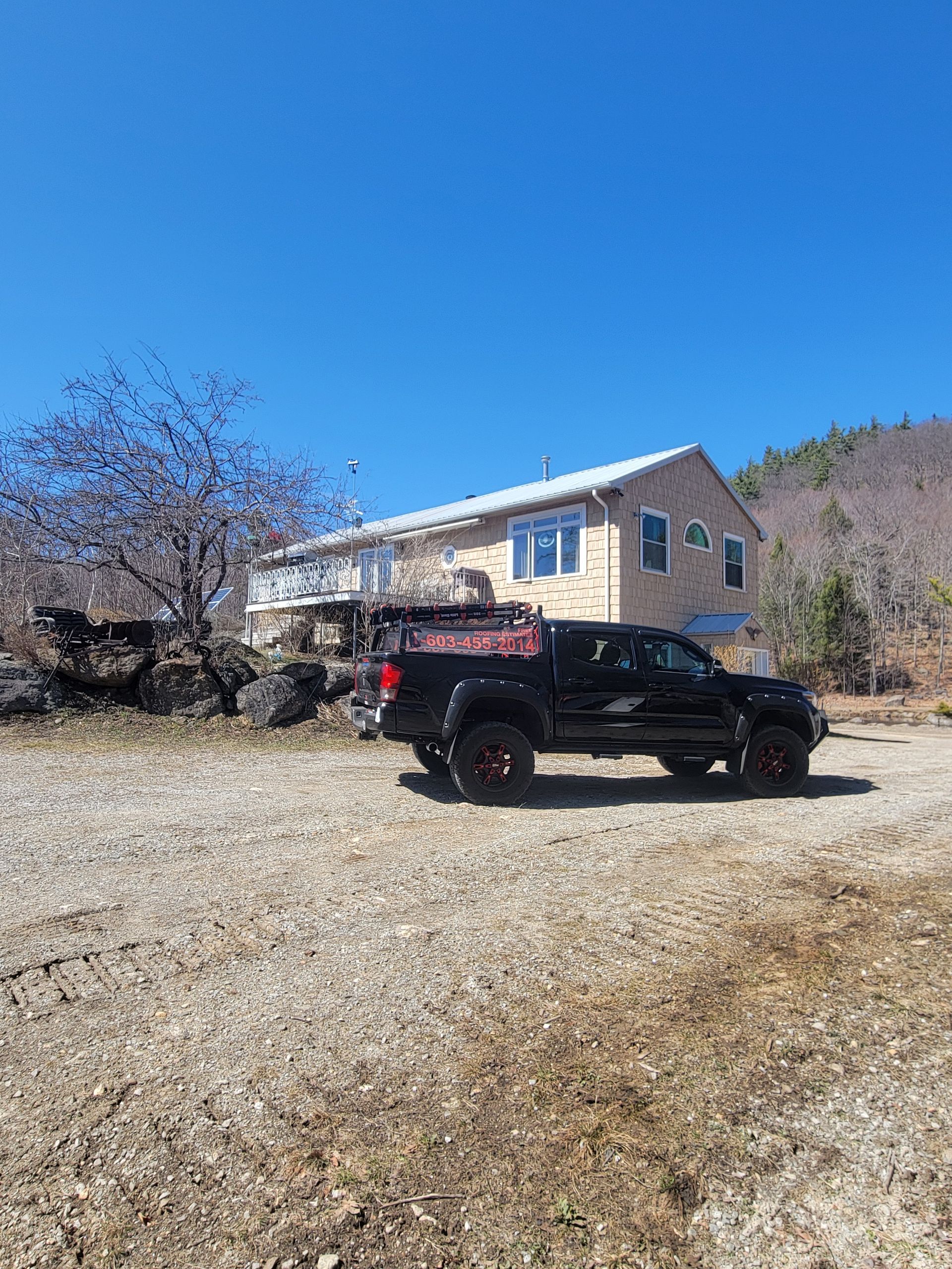 A black truck is parked in a gravel lot in front of a house.