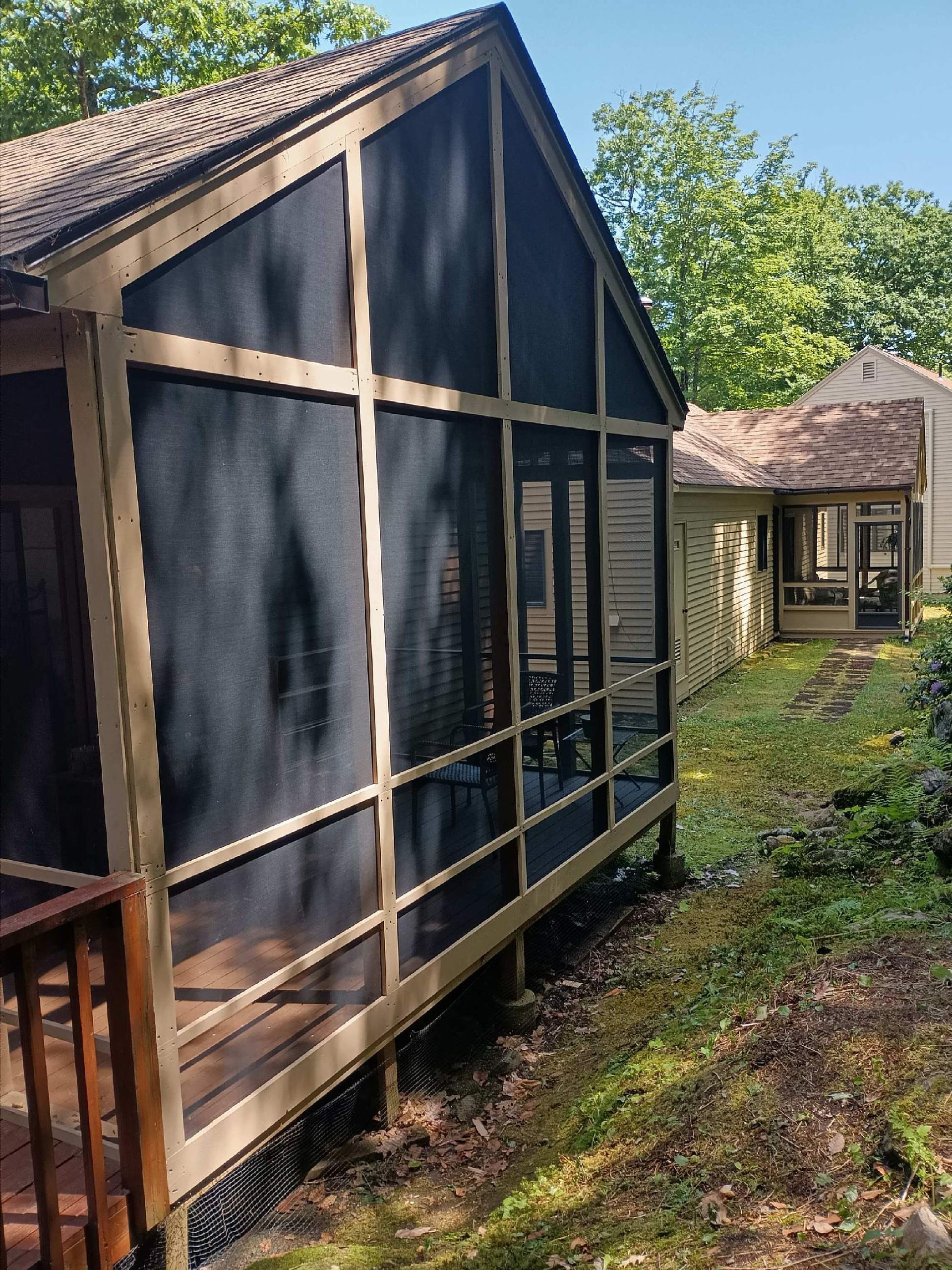 A screened in porch with a wooden deck in front of a house.