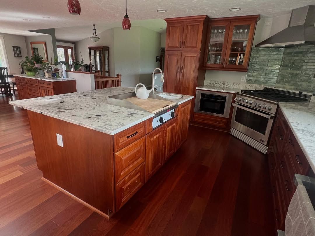 Kitchen with cherry wood cabinets, granite countertops, island with sink, and stainless steel appliances.