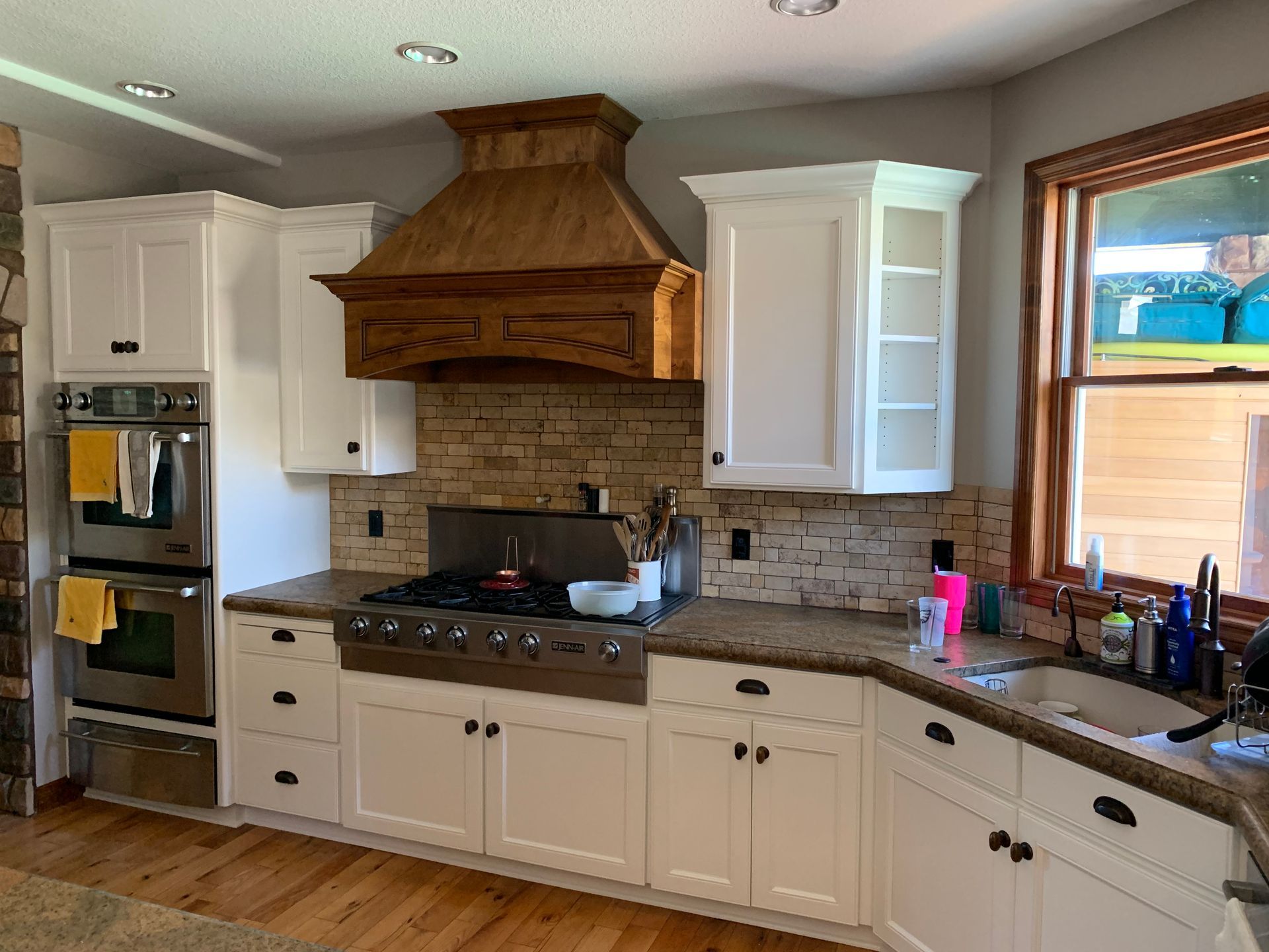 White kitchen with wood hood vent, stone backsplash, and stainless steel appliances.