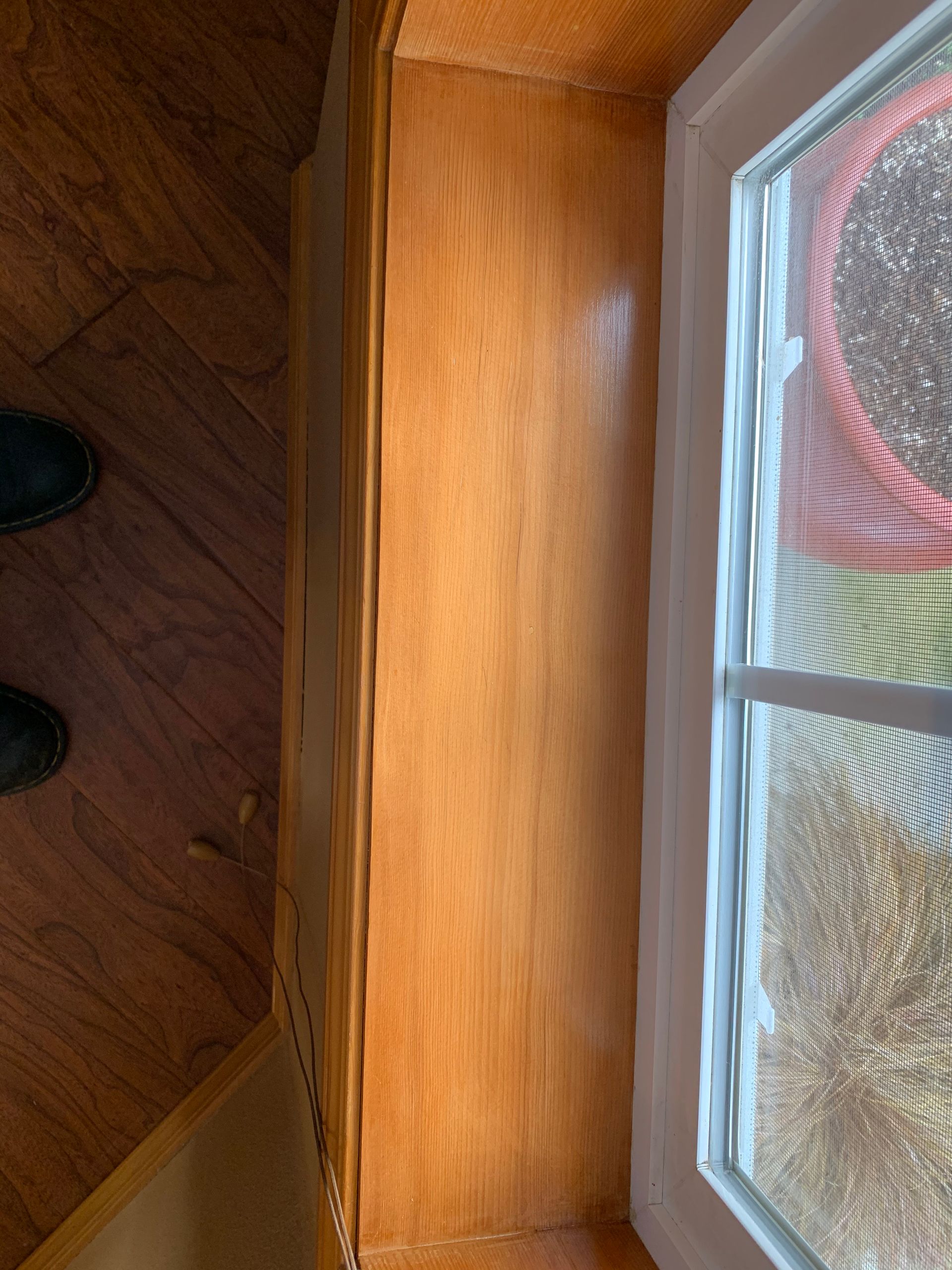 Wooden cabinet next to a window; brown, glossy finish, positioned by a window with white frame.