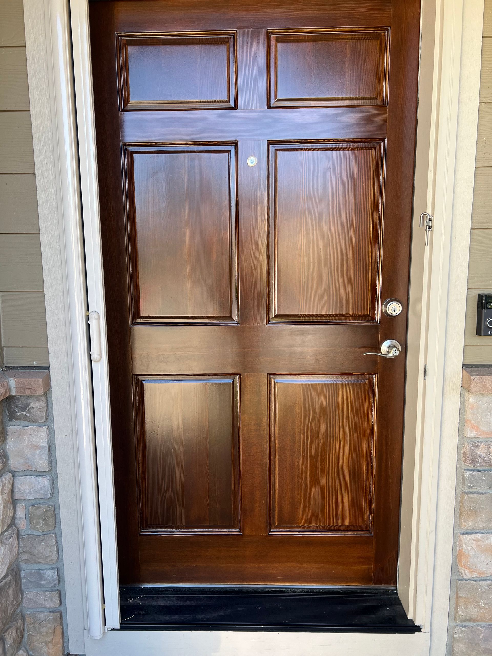 Wooden front door with raised panels, stained dark brown, framed by white trim and stone facade.