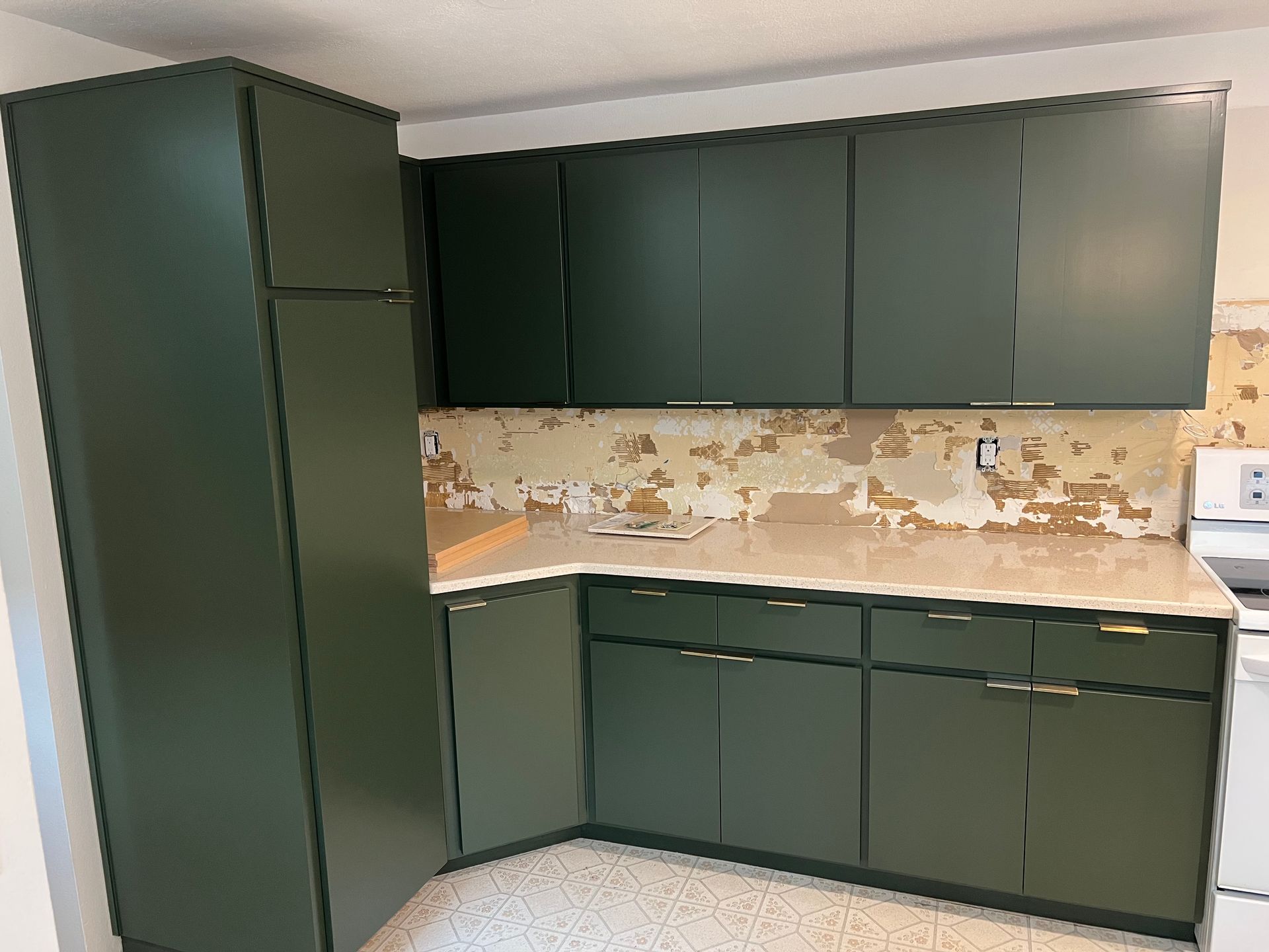 Green kitchen cabinets with a section of damaged backsplash.