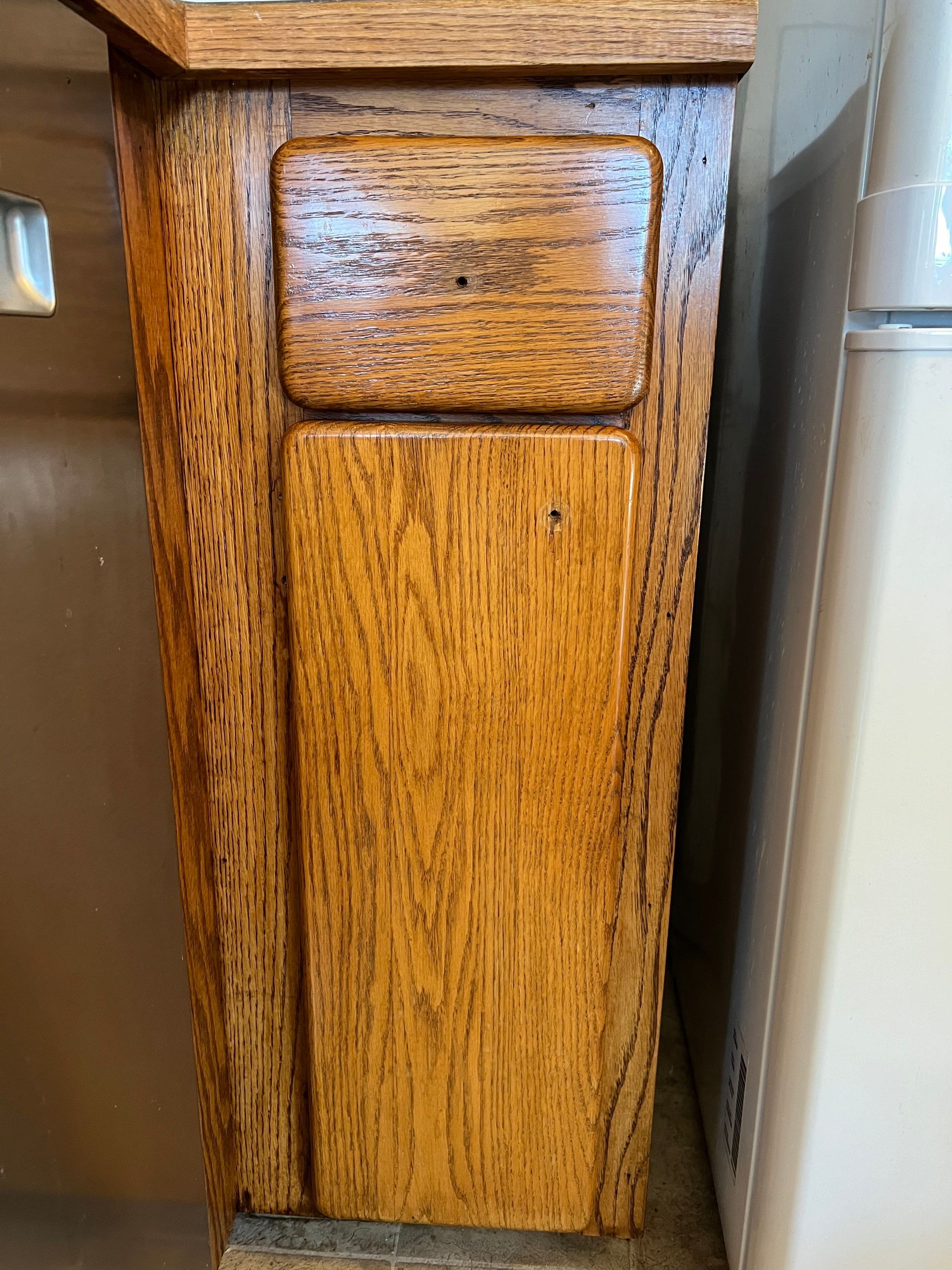 Wooden cabinet, stained oak, with rectangular panel door and upper square detail.
