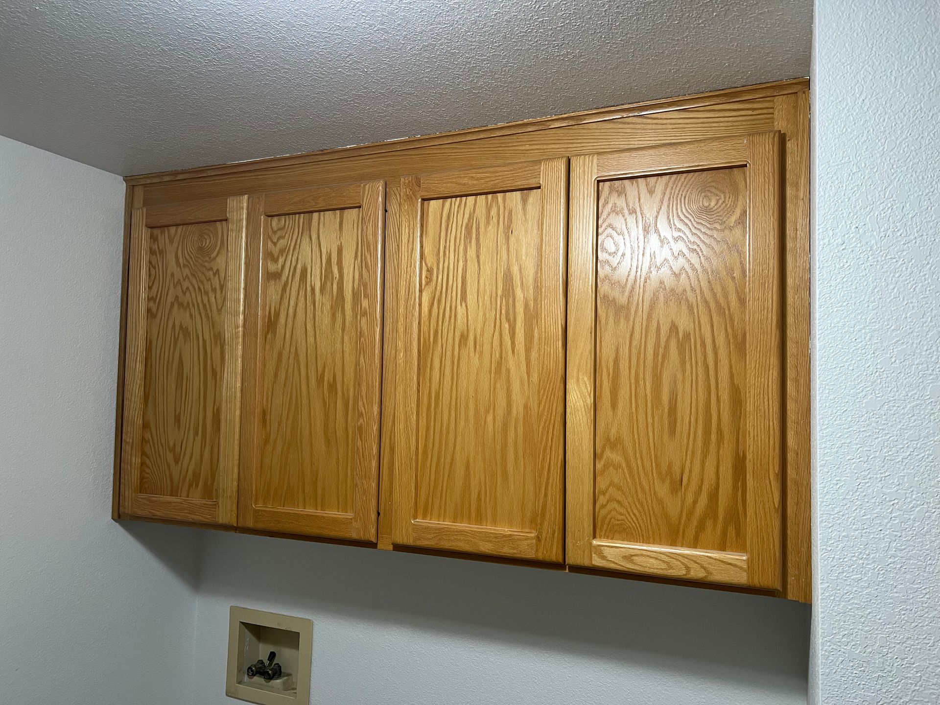 Wooden cabinets mounted above a laundry appliance outlet on a white wall.