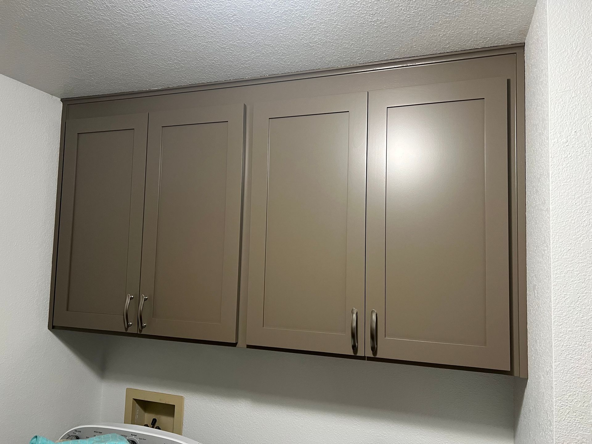 Overhead tan cabinets in a laundry room, with dark handles and a white wall and ceiling.