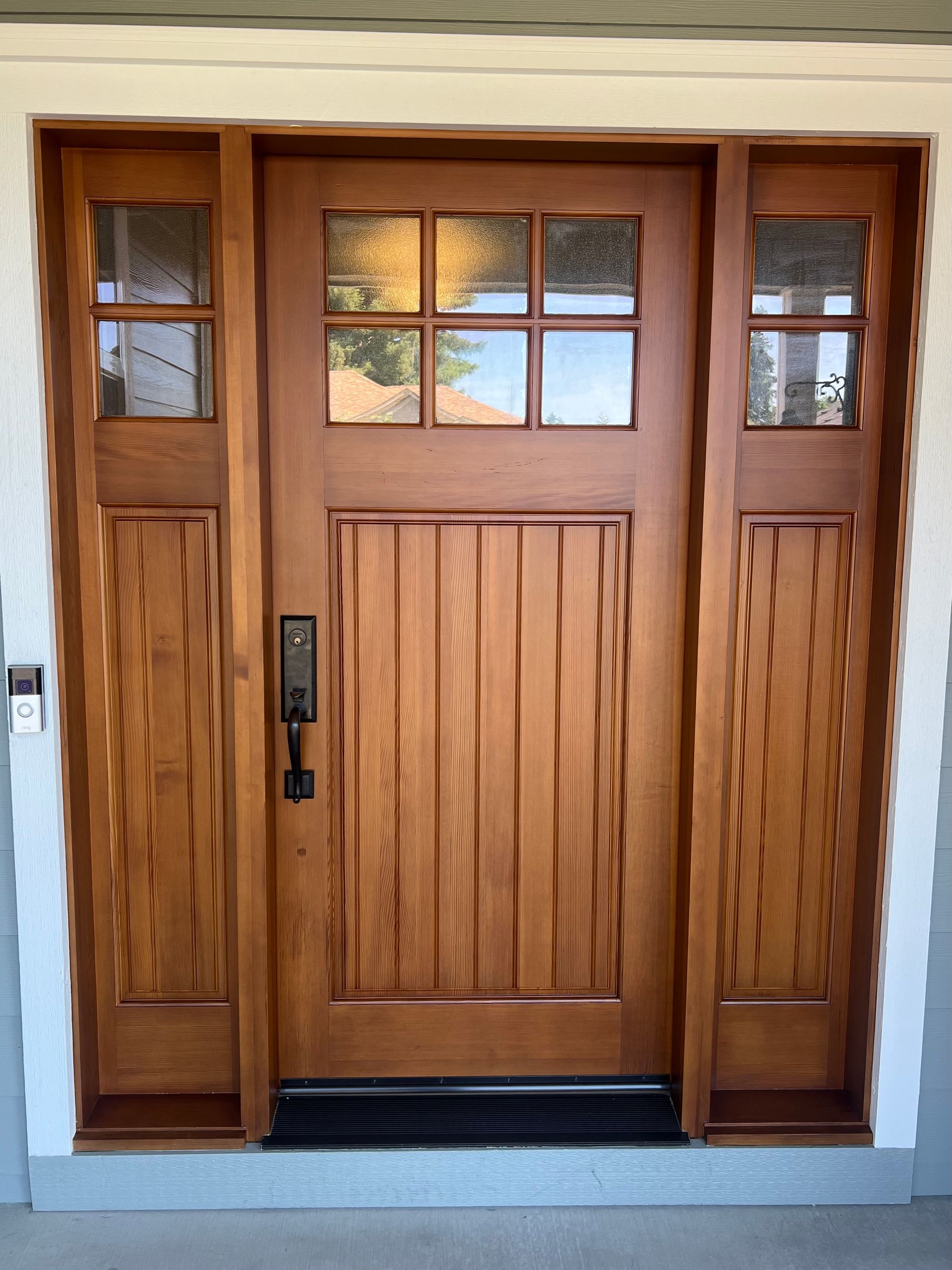 Wooden front door with sidelights, featuring glass panels, and a dark handle.