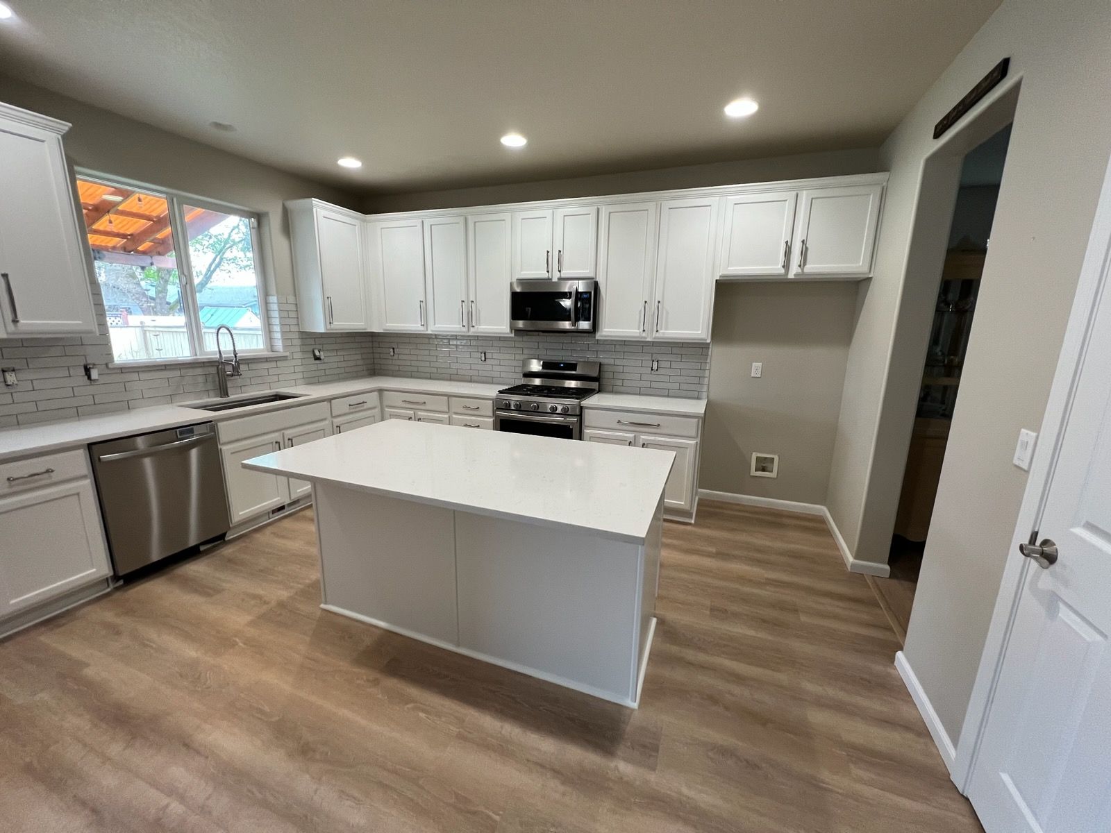 Modern white kitchen with island, stainless steel appliances, and light wood flooring.