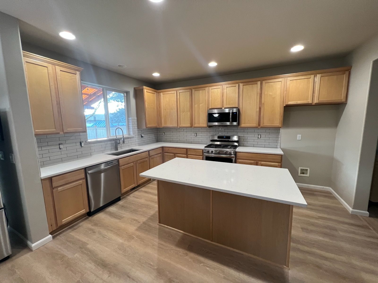 Modern kitchen with light wood cabinets, white countertops, stainless steel appliances, and an island.