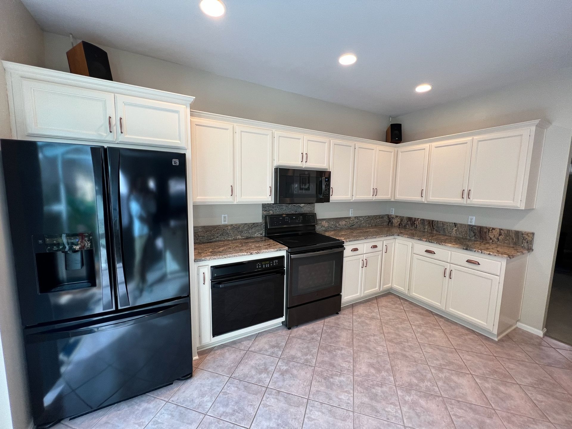 Kitchen with white cabinets, black appliances, and granite countertops. Pink tile floor.