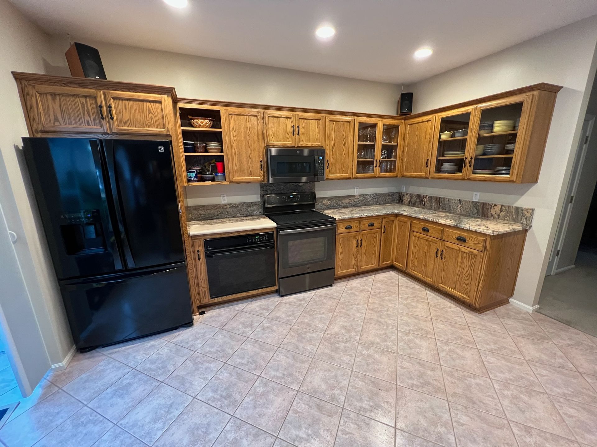 A kitchen with oak cabinets, black appliances, and speckled countertops. The floor is tiled.
