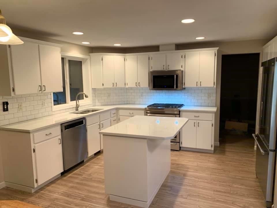White kitchen with island, stainless steel appliances, white cabinets, and wood-look flooring.
