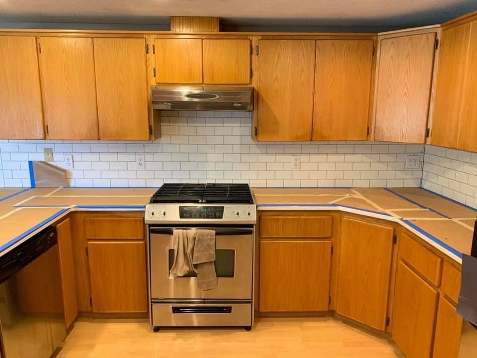 Kitchen with wooden cabinets, stainless steel stove, and white subway tile backsplash under construction, countertop taped.