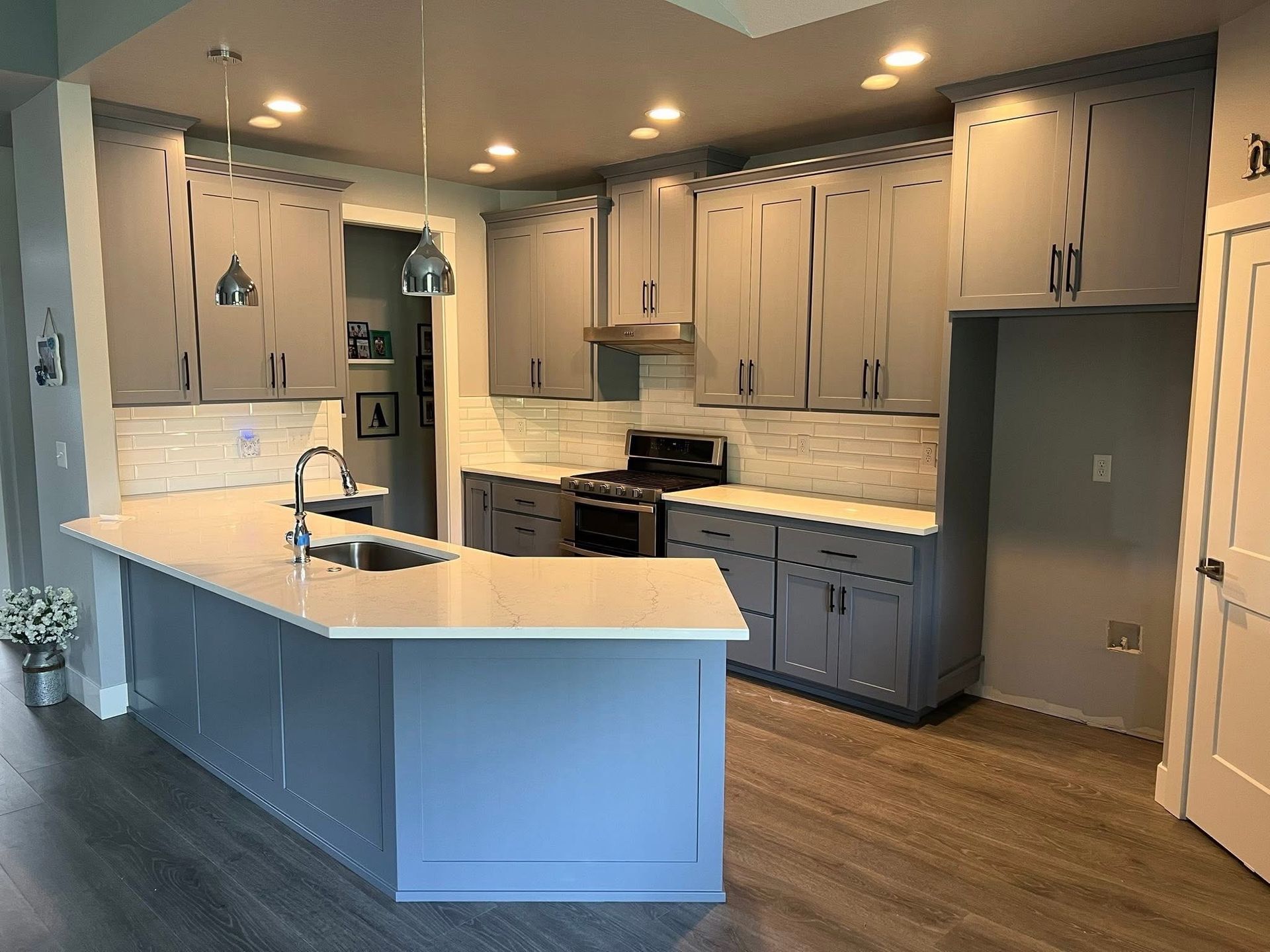 Gray and blue kitchen with island, cabinets, stove, and light wood flooring.