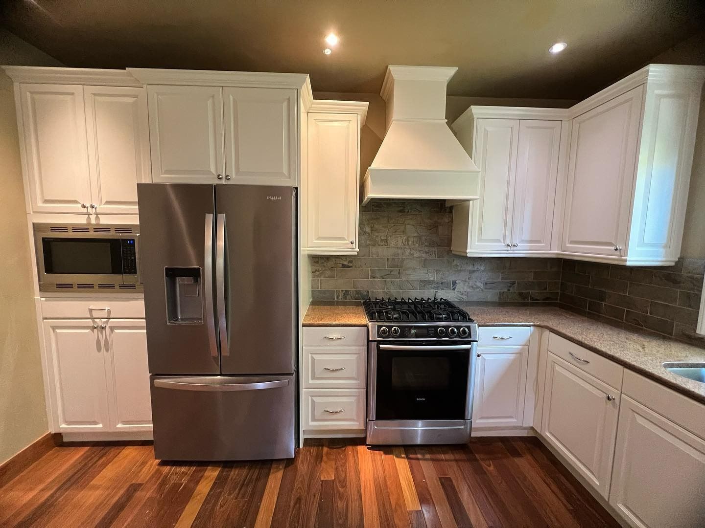 White kitchen with stainless steel appliances, dark wood floor, and beige backsplash.