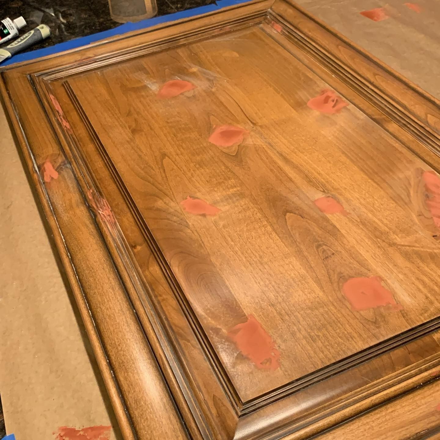 Wooden cabinet door with red wood filler applied to various spots.