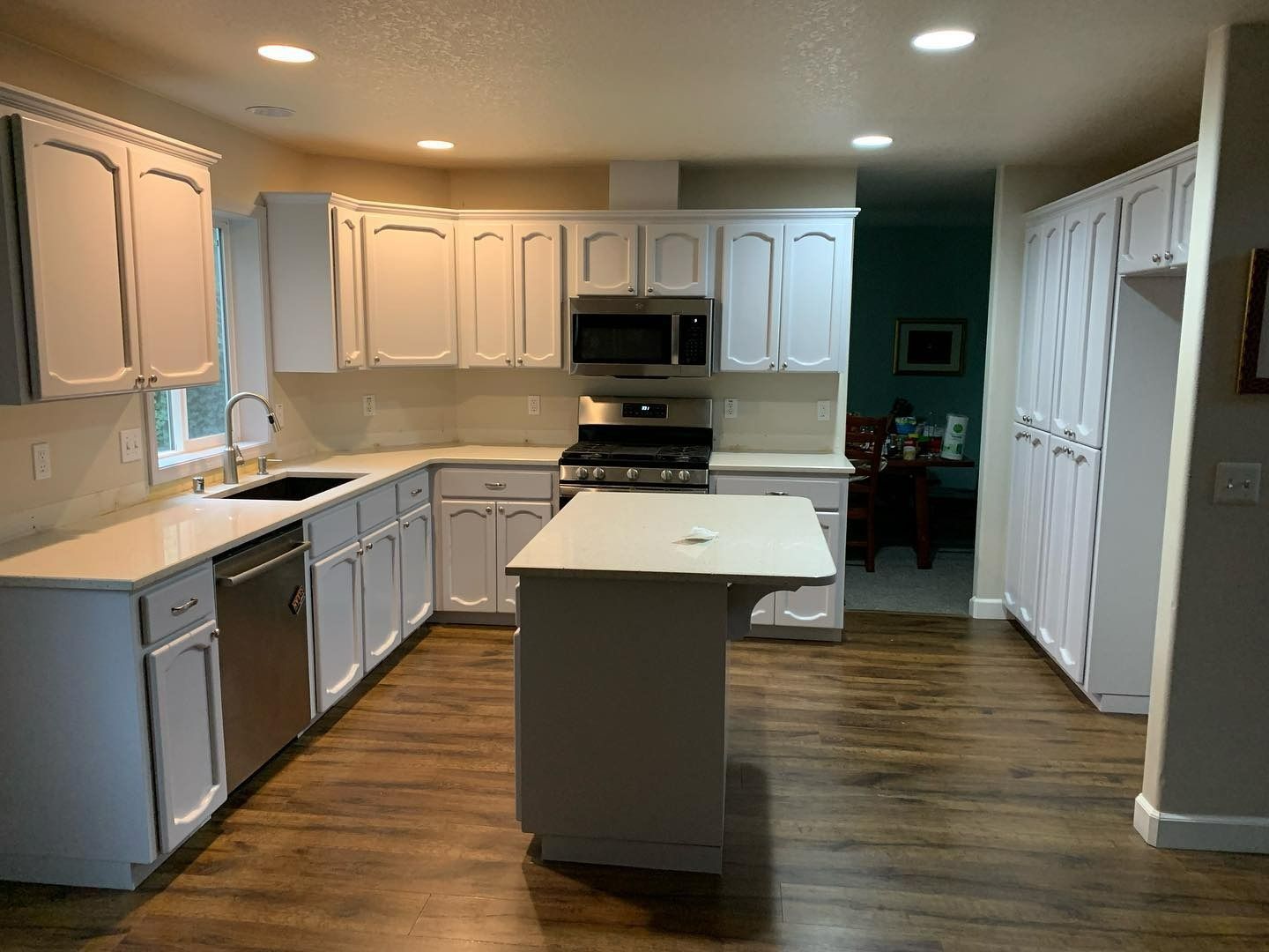 White kitchen with cabinets, island, and appliances on wood-look floors.