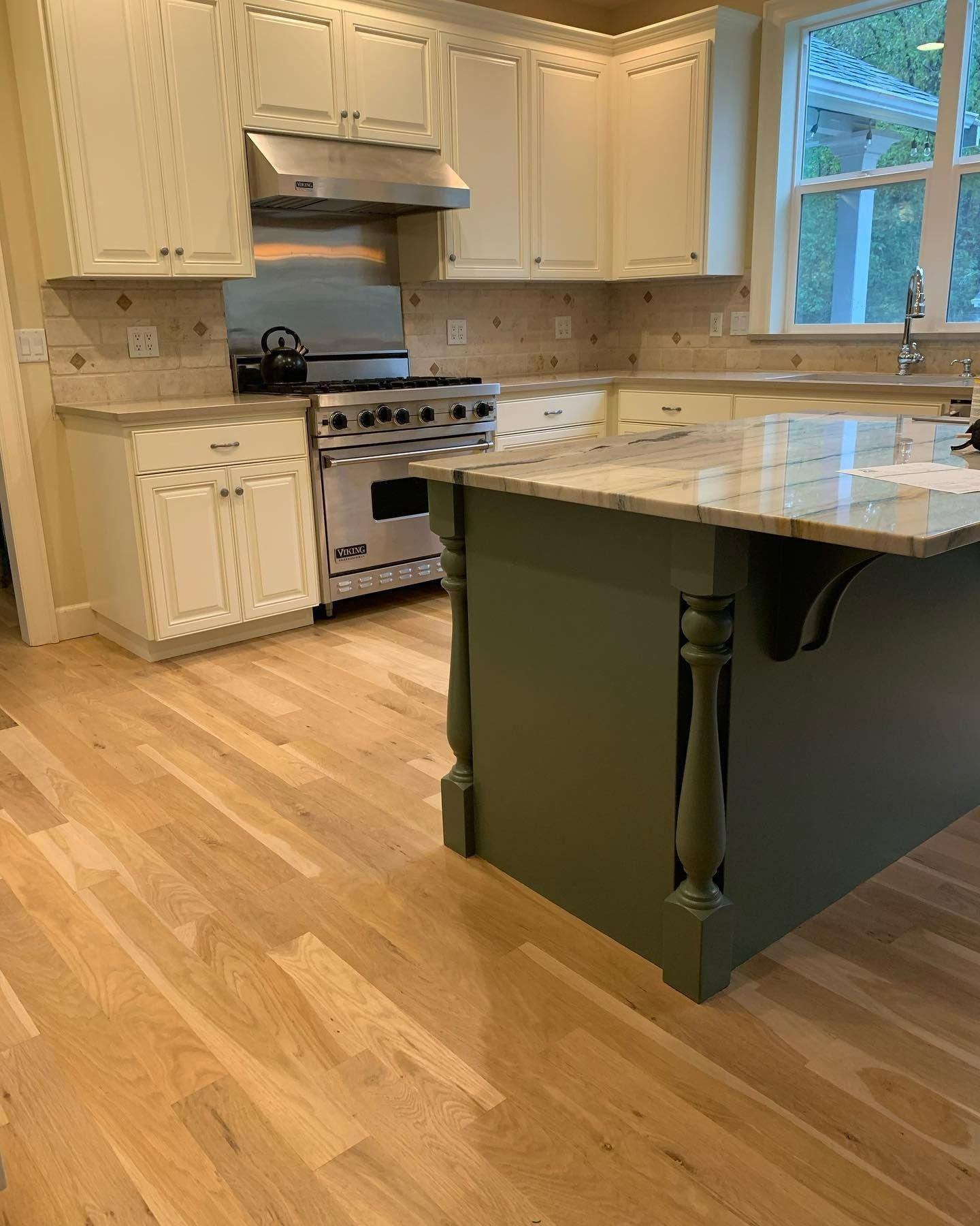 Kitchen with light wood floor, white cabinets, stainless steel appliances, and a green island.