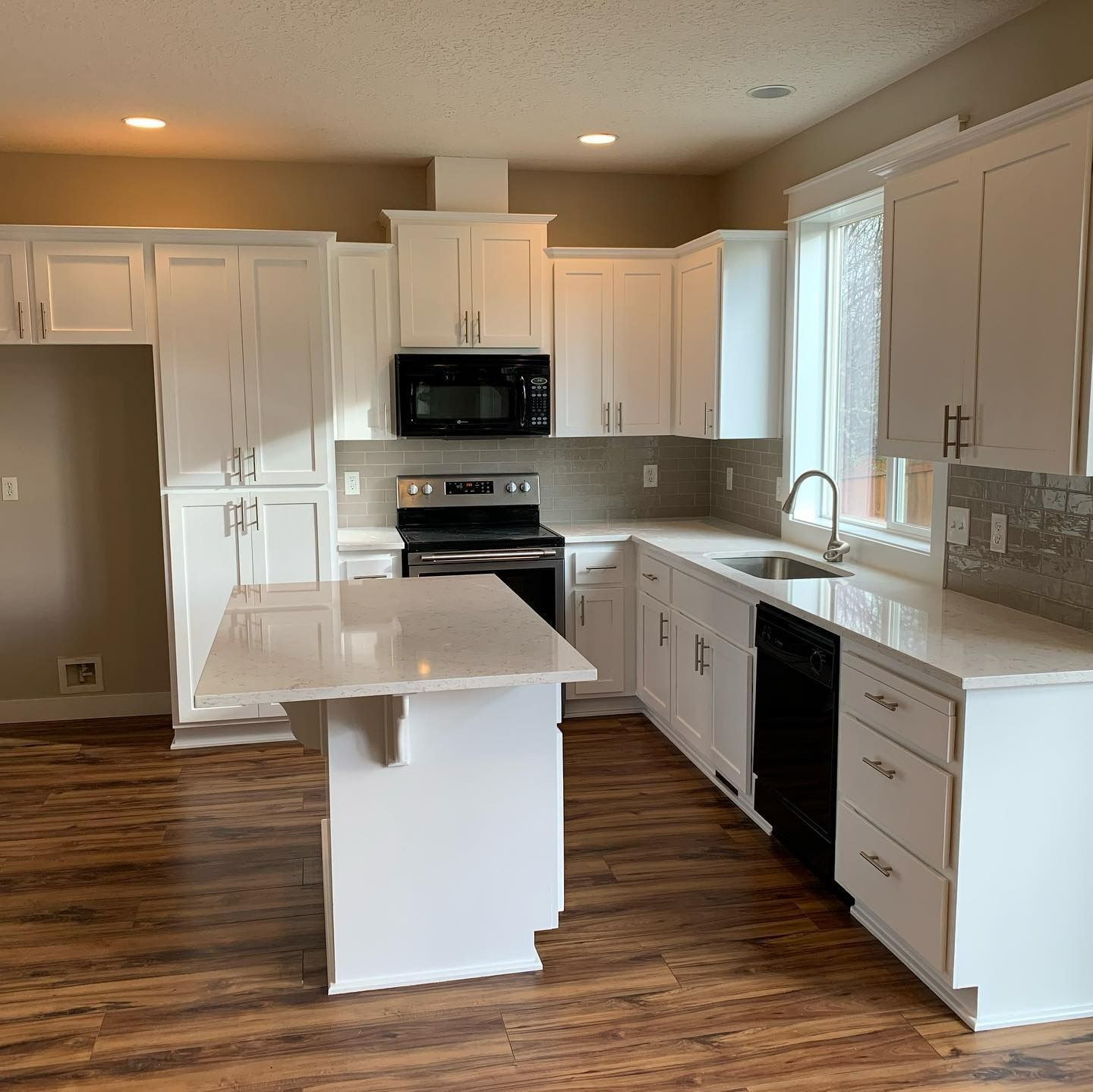 White kitchen with island, cabinets, countertops, and appliances, on wood-look flooring.