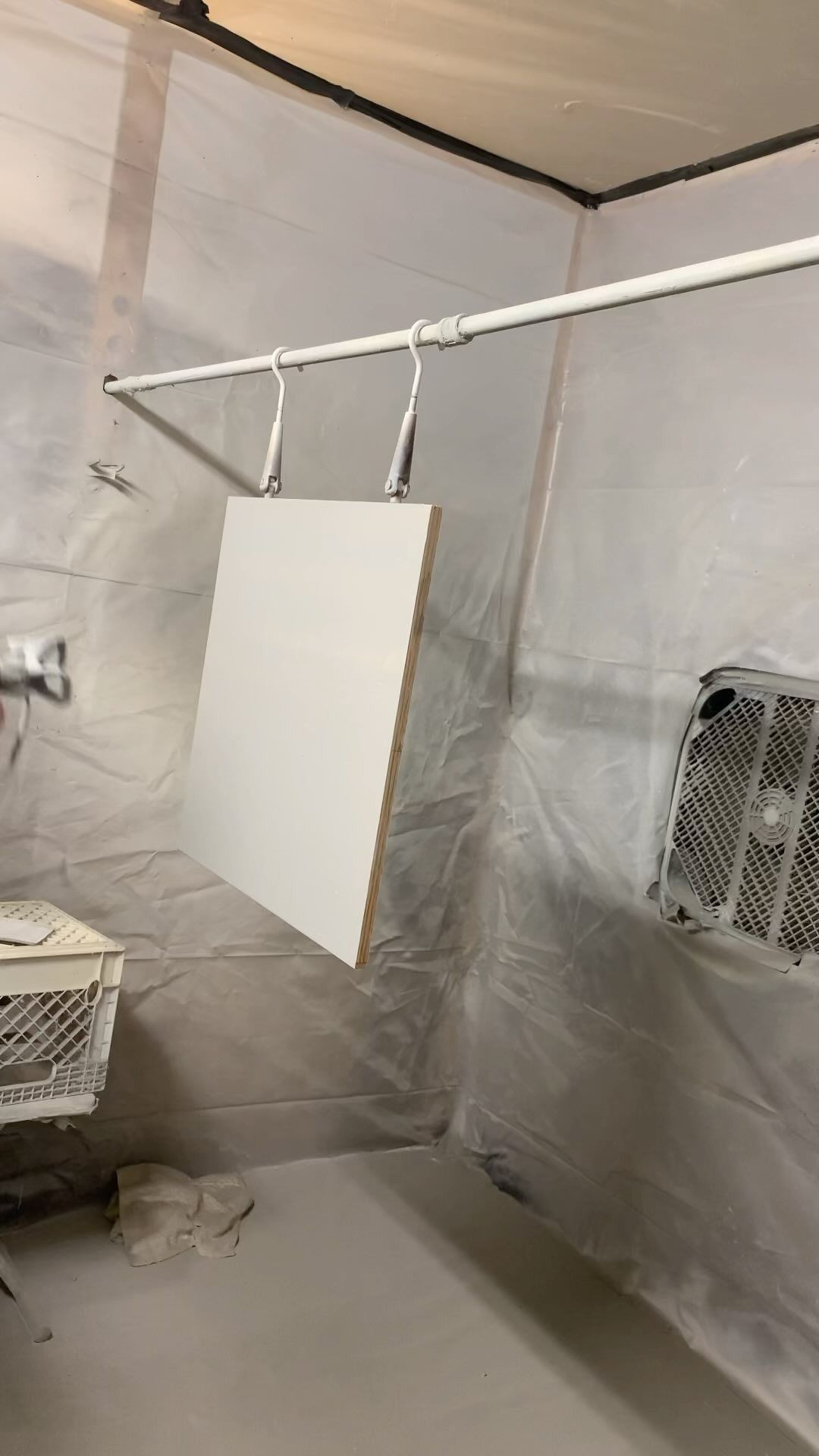 A white square panel hanging from a rod inside a spray booth for painting.