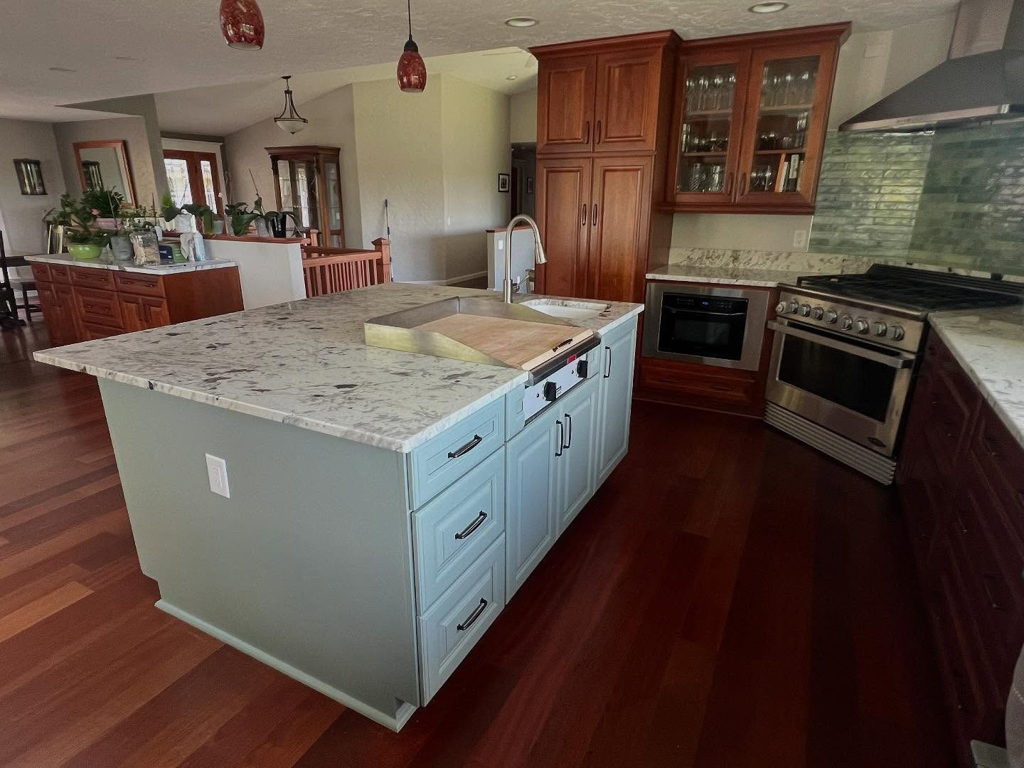 Kitchen with blue island, granite countertop, stainless steel appliances, and dark wood floors.