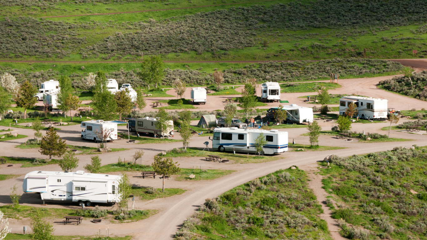 RV campground in a grassy valley with several RVs parked at sites. Dirt roads and small trees are visible.