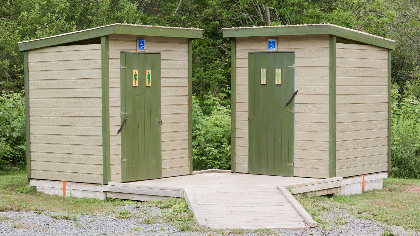 Two outdoor public restrooms with green doors and blue gender symbols. One has a ramp for accessibility.